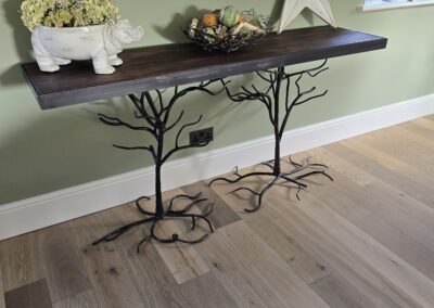 Dark wooden console table with black iron branch legs stands against a sage green wall, topped with a star, a ceramic planter, and a wire fruit bowl.